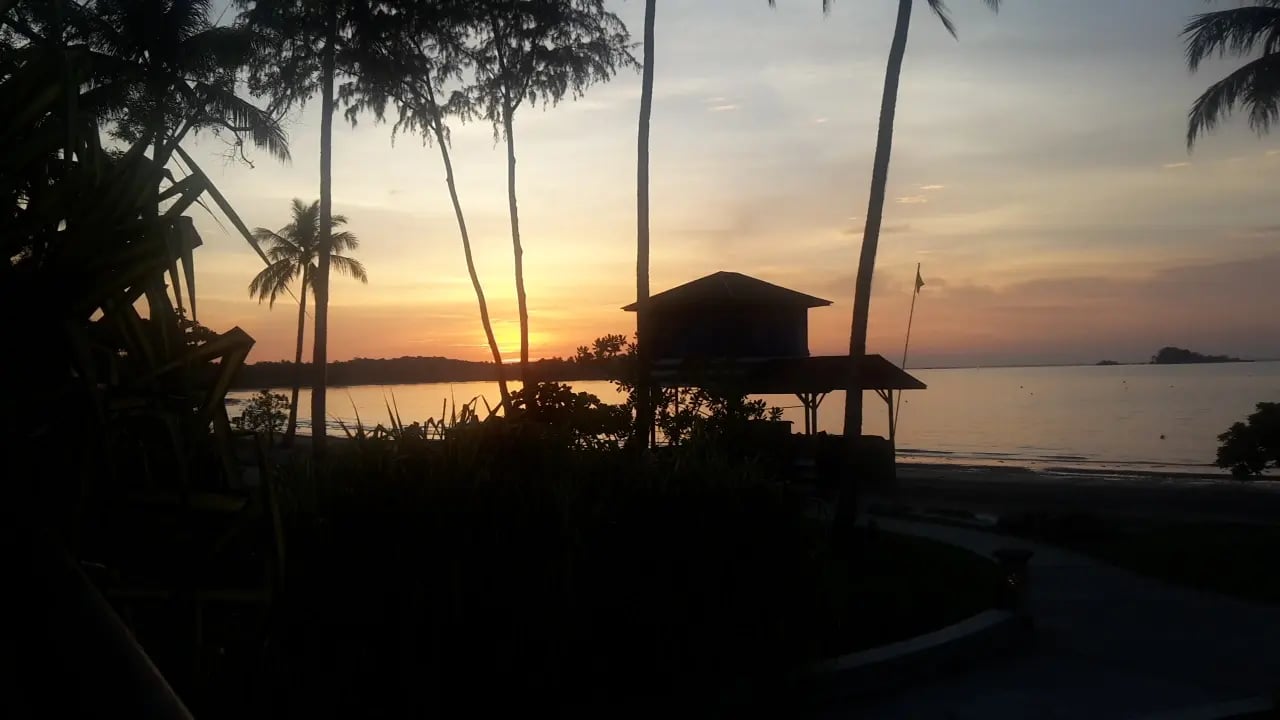Sonnenuntergang am Strand in Malaysia mit Palmen und einer kleinen Hütte.