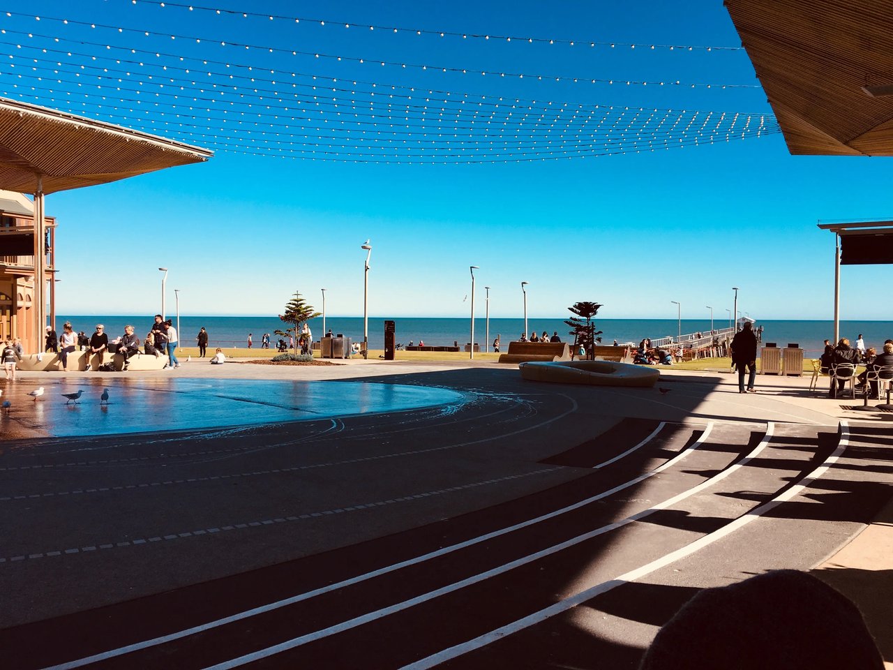 Henley Beach Strandpromenade in Adelaide mit Sonnensegeln und Lichterkette bei Sonnenuntergang.