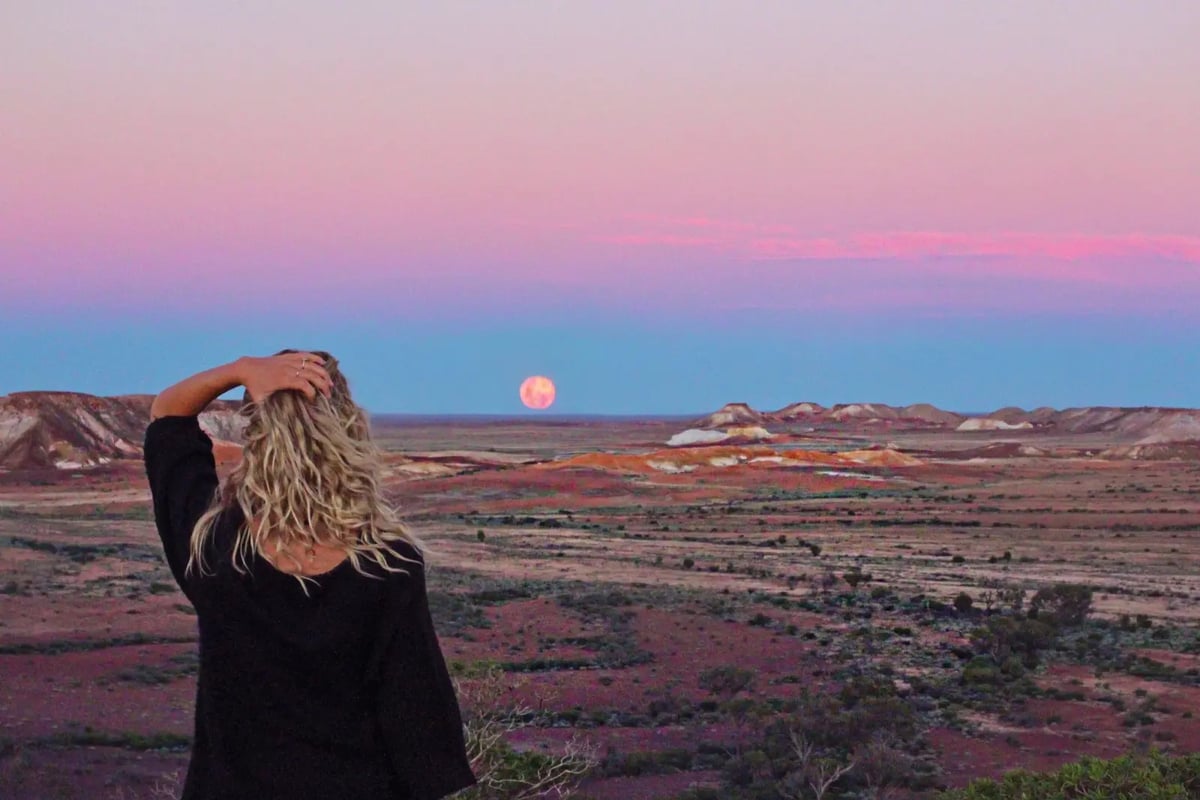 Studentin blickt bei Sonnenuntergang über die farbenfrohe Wüstenlandschaft in Australien – magischer Moment während des Auslandssemesters.