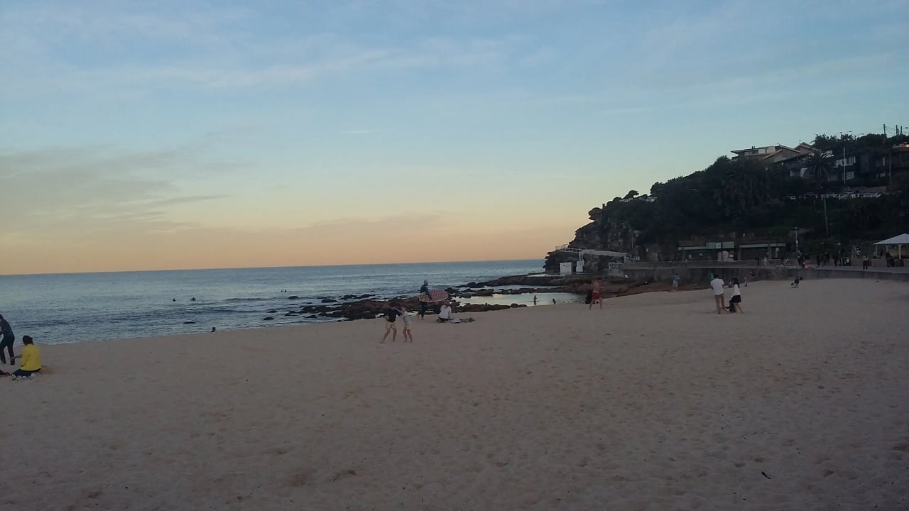Strand in Sydney während des Sonnenuntergangs mit wenigen Menschen im Sand.