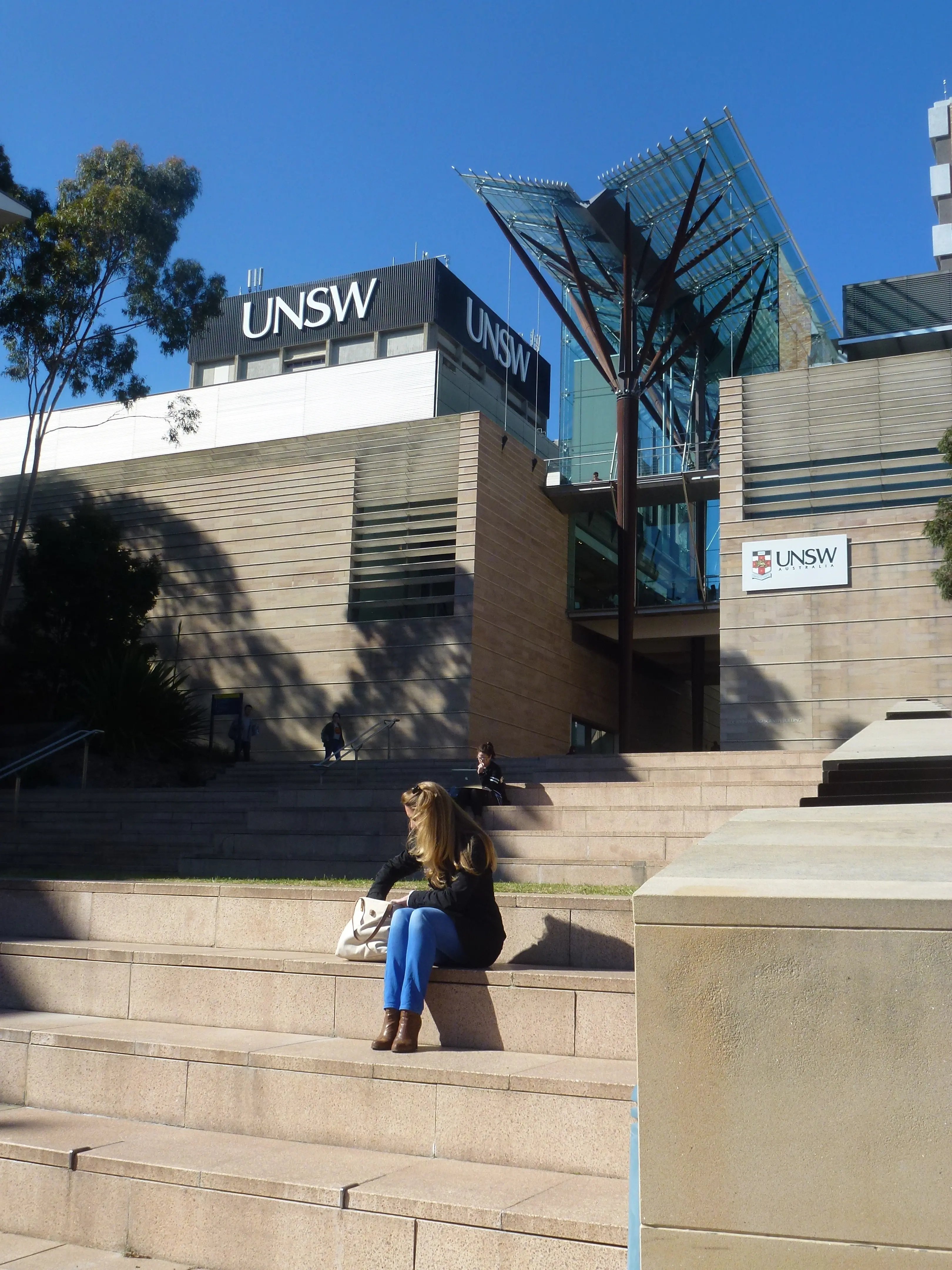 Treppenbereich auf dem Campus der University of New South Wales mit moderner Architektur, grünen Elementen und Studierenden, die auf den Stufen sitzen. 