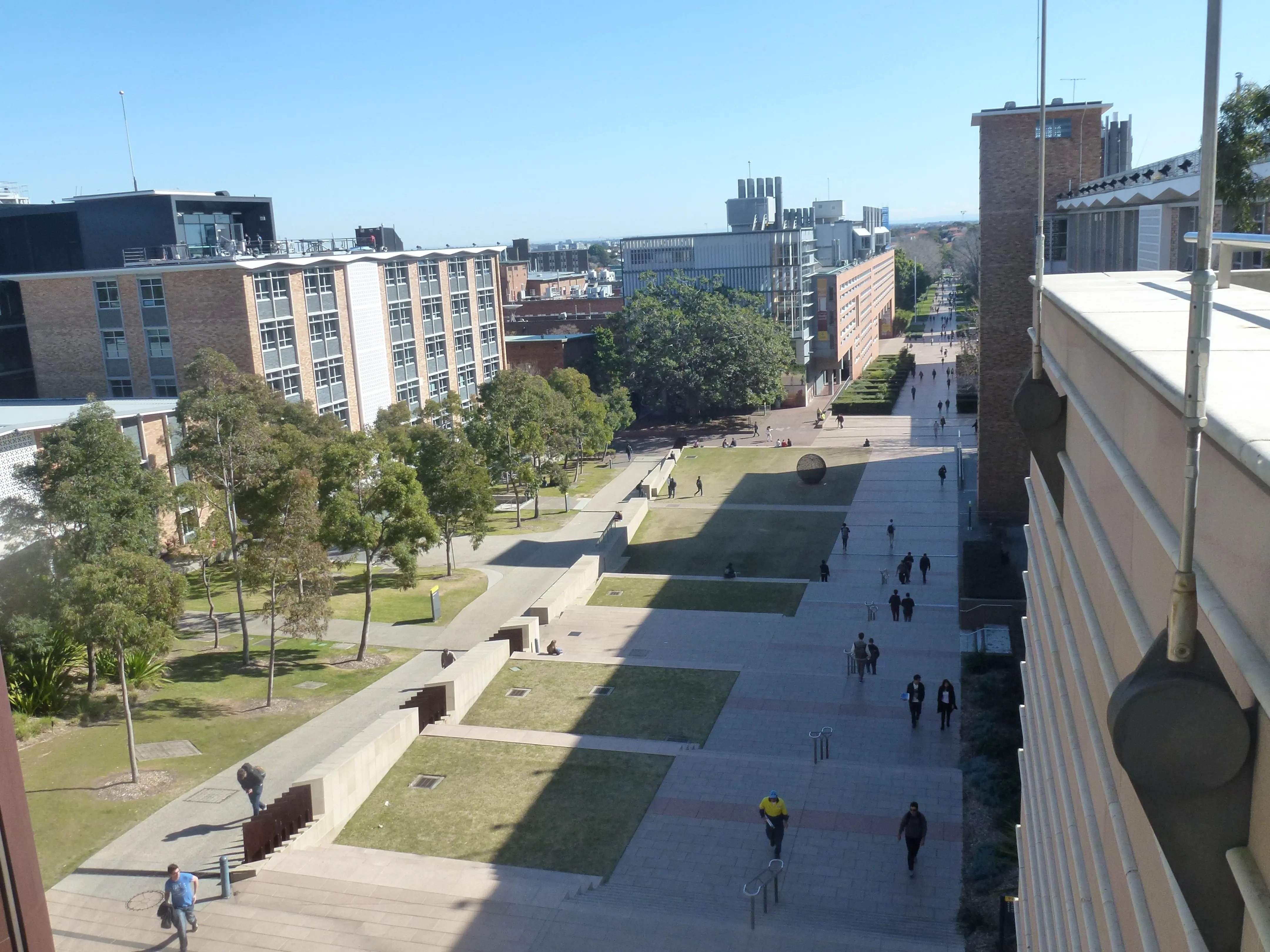 Campus der University of New South Wales mit modernen Gebäuden, begrünten Wegen und Studierenden, die auf dem Hauptweg unterwegs sind. 