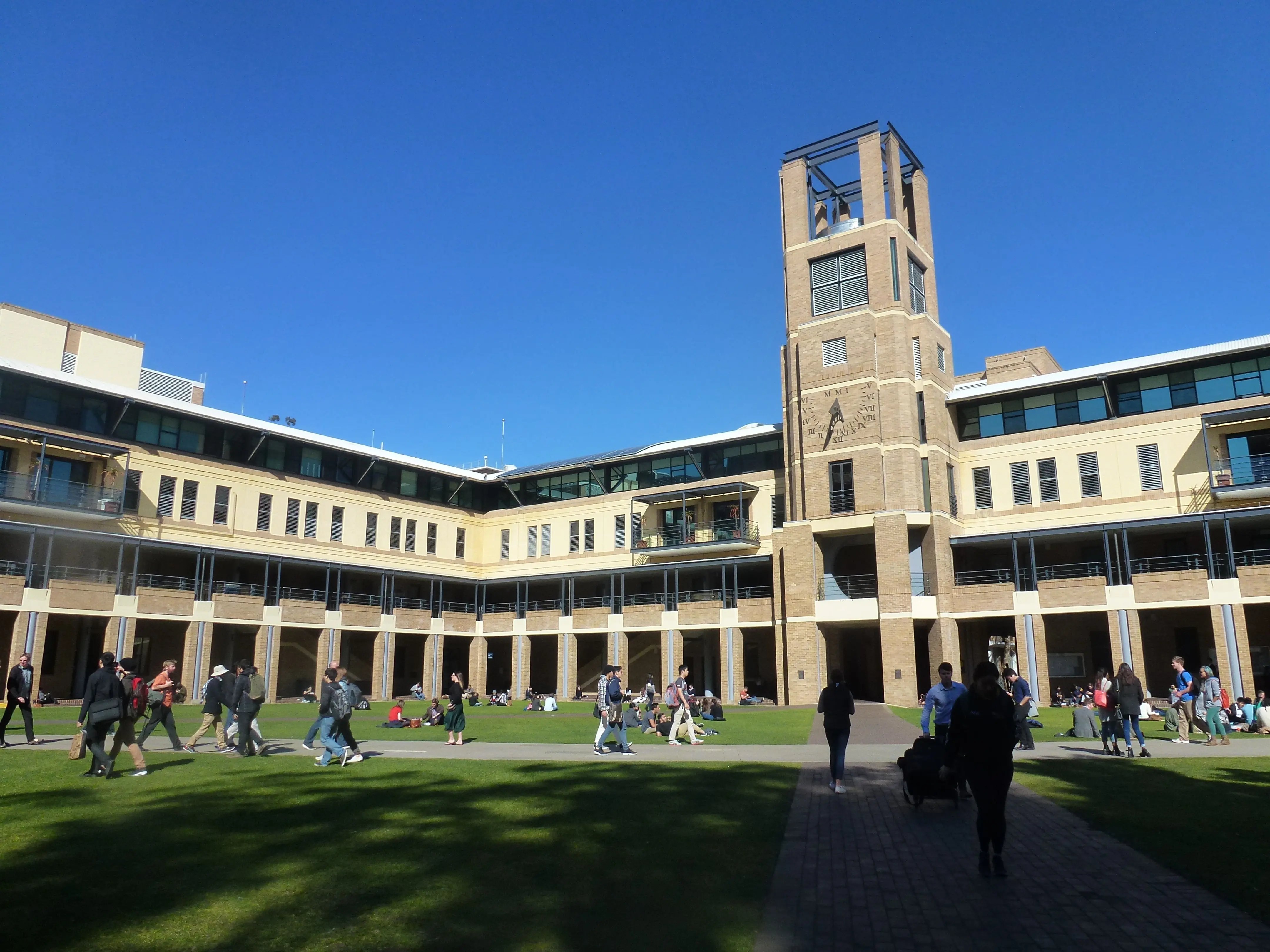 Hauptgebäude der University of New South Wales mit markantem Turm, umgeben von Studierenden, die auf dem Campus unterwegs sind oder auf der Wiese entspannen.