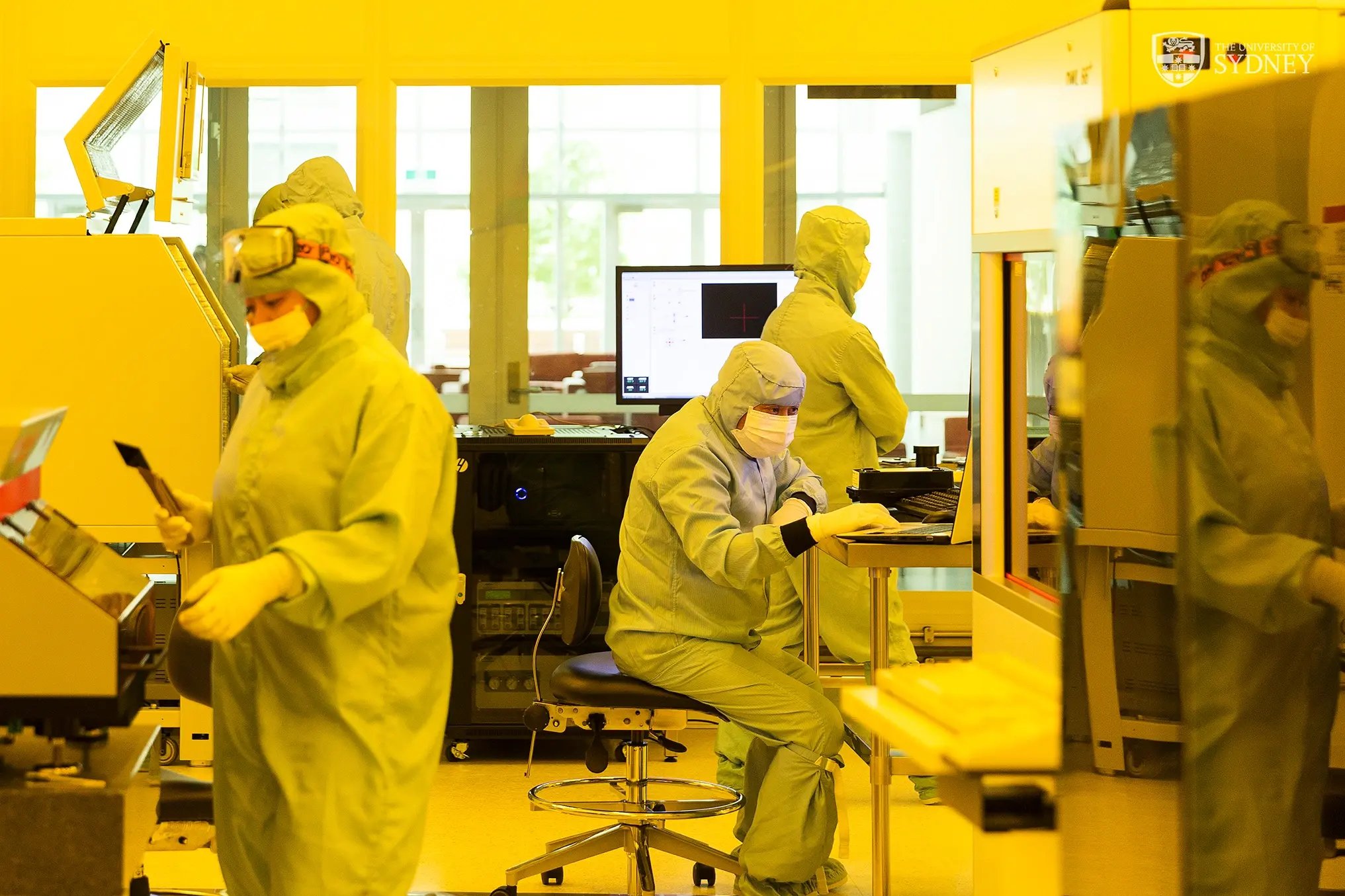 Forschende Studierende in Schutzanzügen arbeiten in einem hochmodernen Labor. 