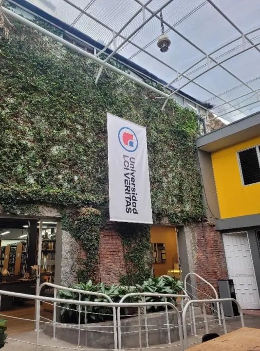 Eine mit Pflanzen bewachsene Ziegelwand mit einem großen Universitätsbanner und einer offenen Bibliothek im Hintergrund.