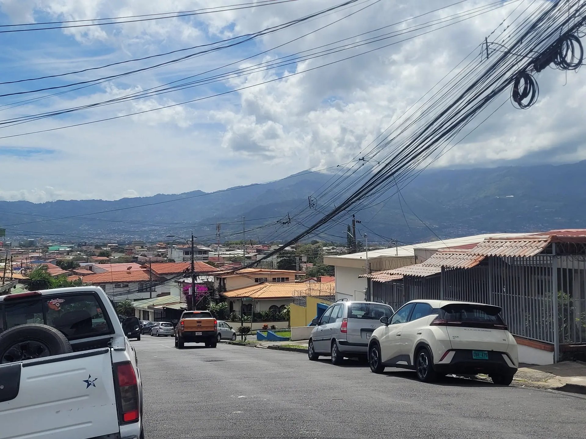 Eine Wohnstraße mit bunten Häusern, geparkten Autos und einem weiten Blick auf die grünen Berge im Hintergrund.