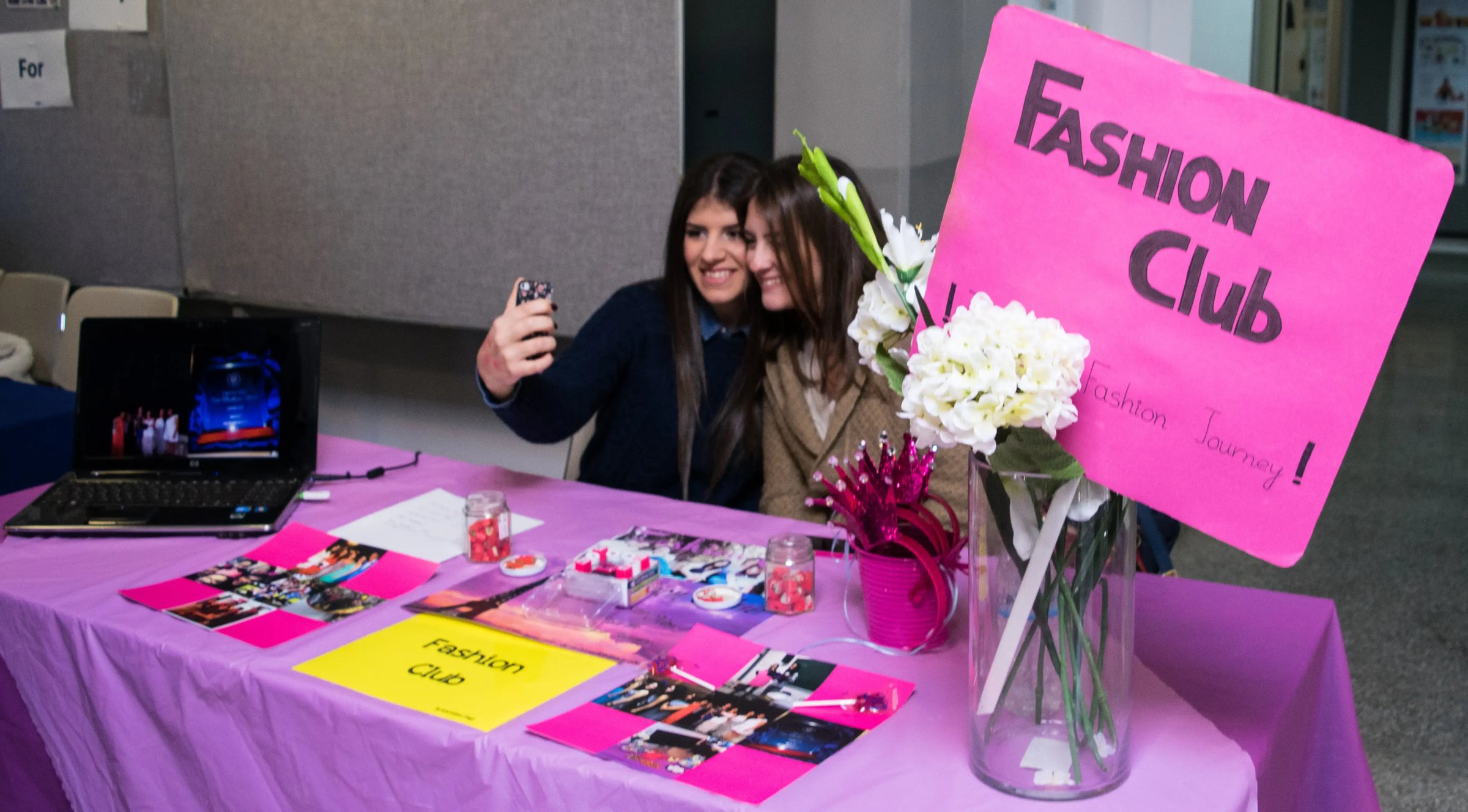 Studentin macht ein Selfie am bunt dekorierten Stand des Fashion Clubs.
