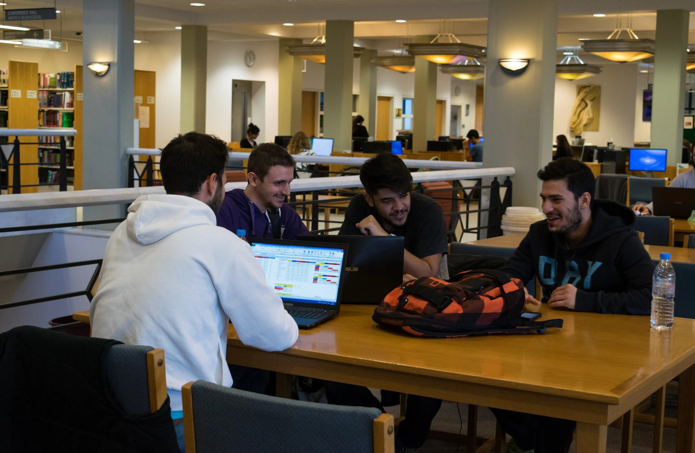 Studierende arbeiten gemeinsam mit Laptops an einem Tisch in einer Bibliothek