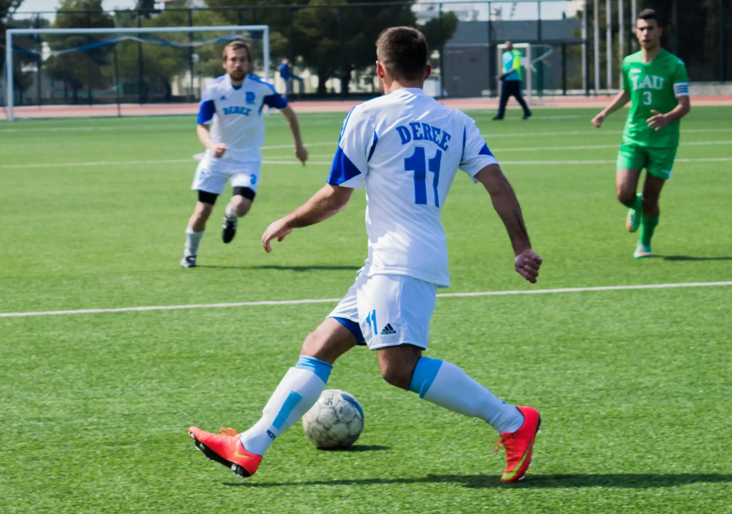 Student im weißen Trikot beim Fußballspiel auf dem Campus. 