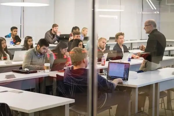 Ein Universitätsseminar mit Studierenden, die aufmerksam einem Professor zuhören. Die moderne Unterrichtsumgebung ist mit Laptops und Notizbüchern ausgestattet.