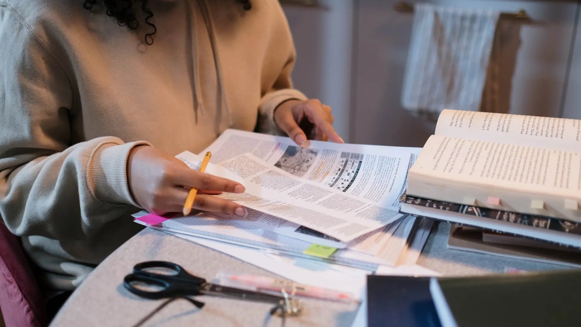 Person sitzt mit Unterlagen, Büchern und Schreibuntensilien am Tisch und lernt