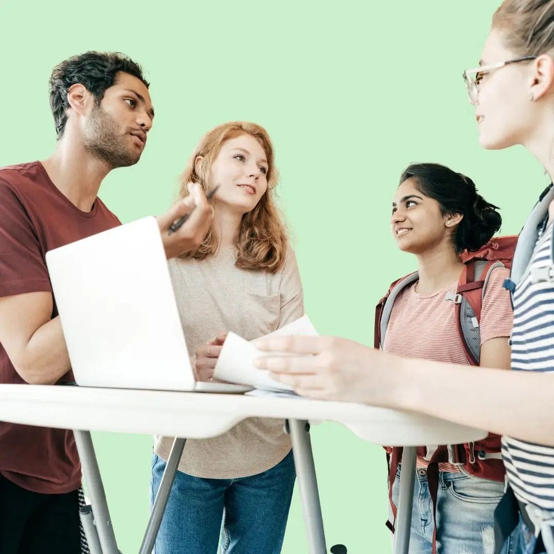 Gruppe internationaler Studierender im Gespräch an einem Stehtisch mit Laptop und Unterlagen – Austausch und Planung für ein Auslandssemester.