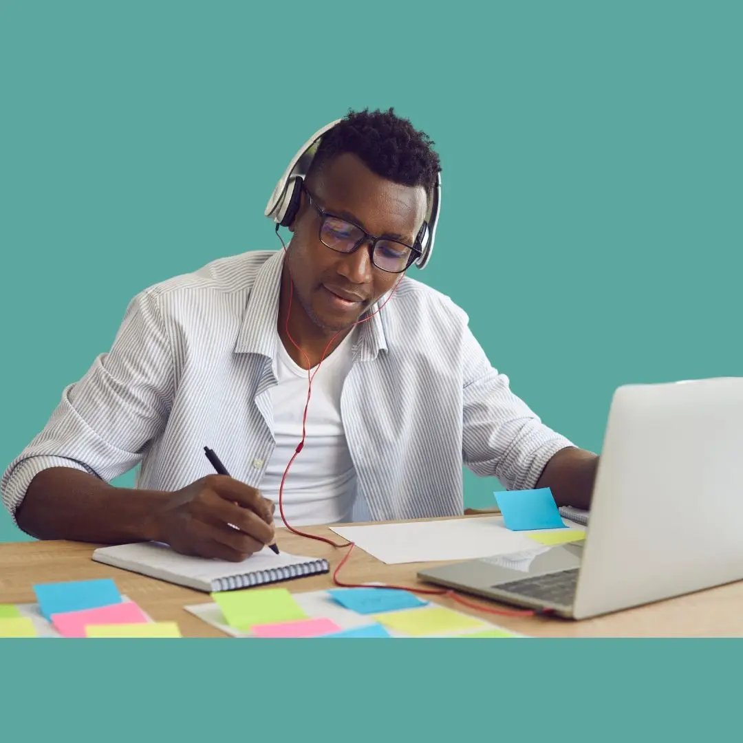 Student mit Kopfhörern sitzt vor einem Laptop und macht Notizen. 