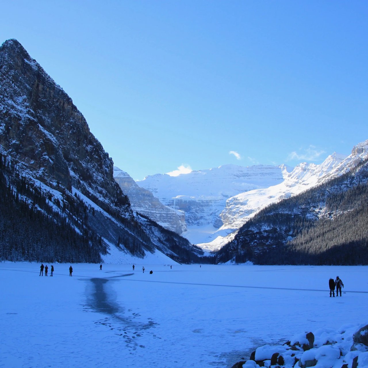 Verschneite Berglandschaft der Rocky Mountains mit einem zugefrorenen See und Wanderern.