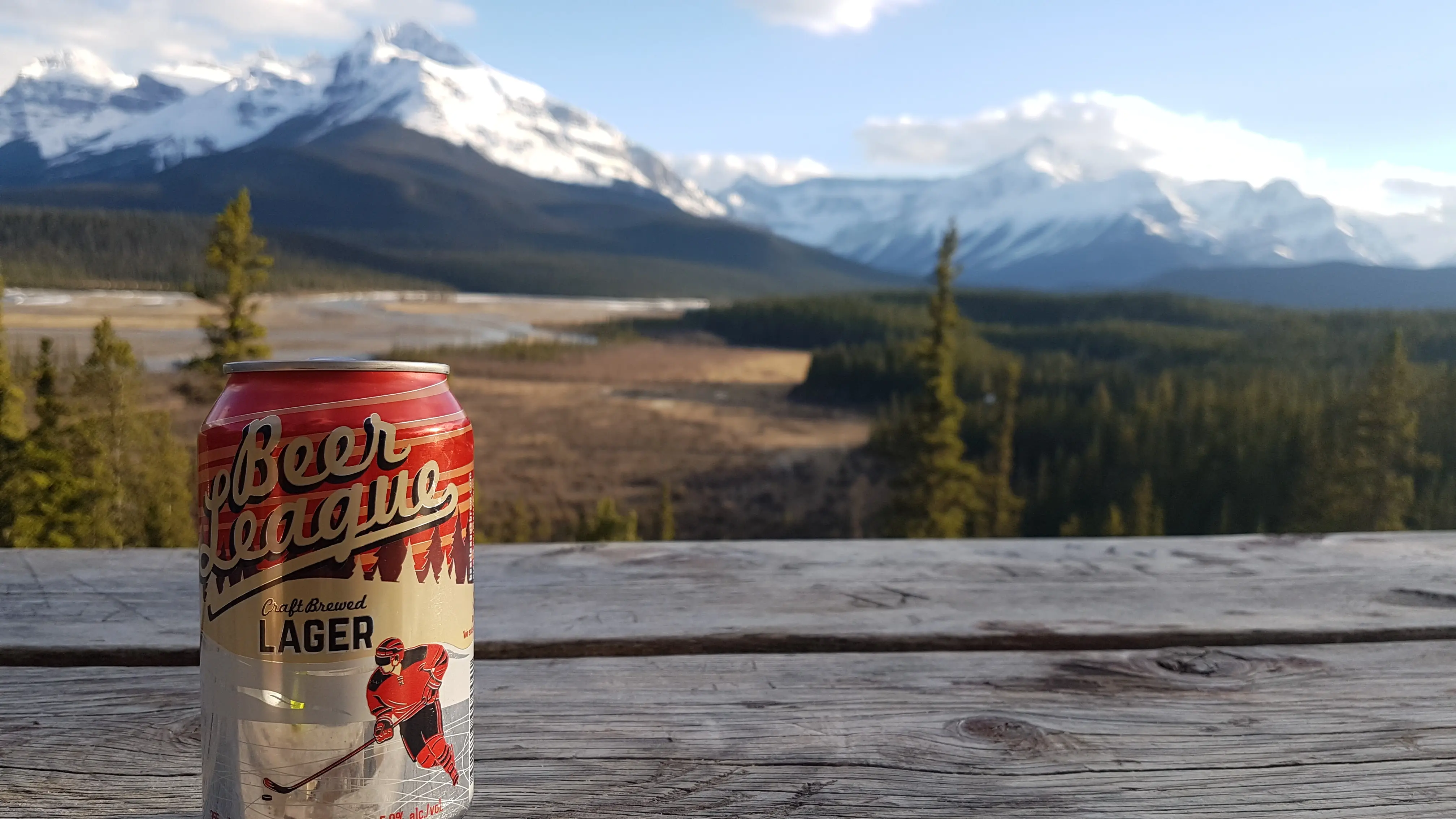 Bierdose auf einem Holztisch mit Blick auf schneebedeckte Berge in Kanada.