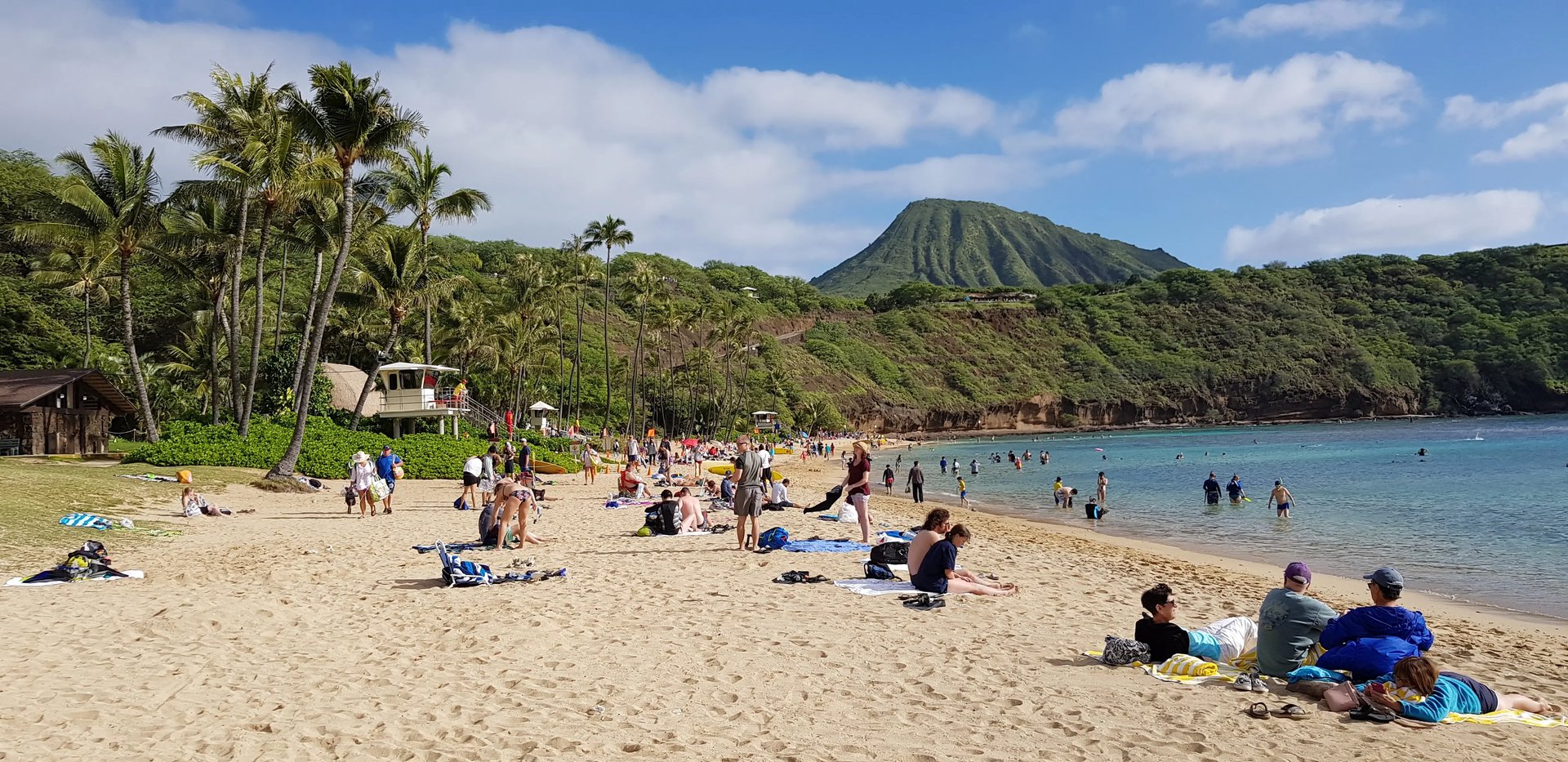 Ausflug zu einem beliebten Strand in Hawaii mit Blick auf den Diamond Head Krater und vielen Menschen, die das Wasser genießen.