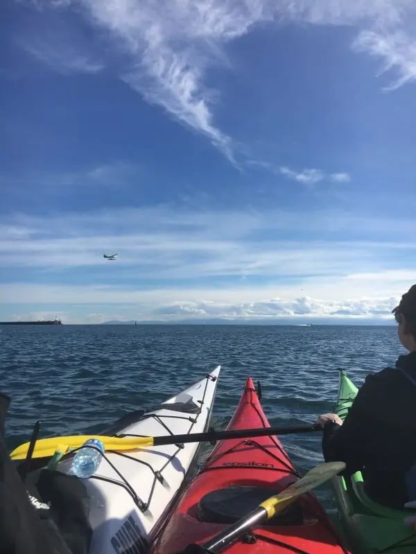 Kajaktour auf dem offenen Meer in der Nähe von Victoria, Kanada, mit blauem Himmel und einem Flugzeug am Horizont.