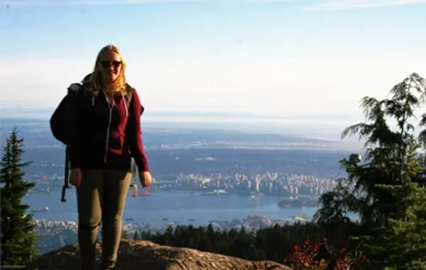 Studentin der British Columbia Institute of Technology mit Rucksack genießt die Aussicht auf die Stadt Vancouver von einem Berggipfel