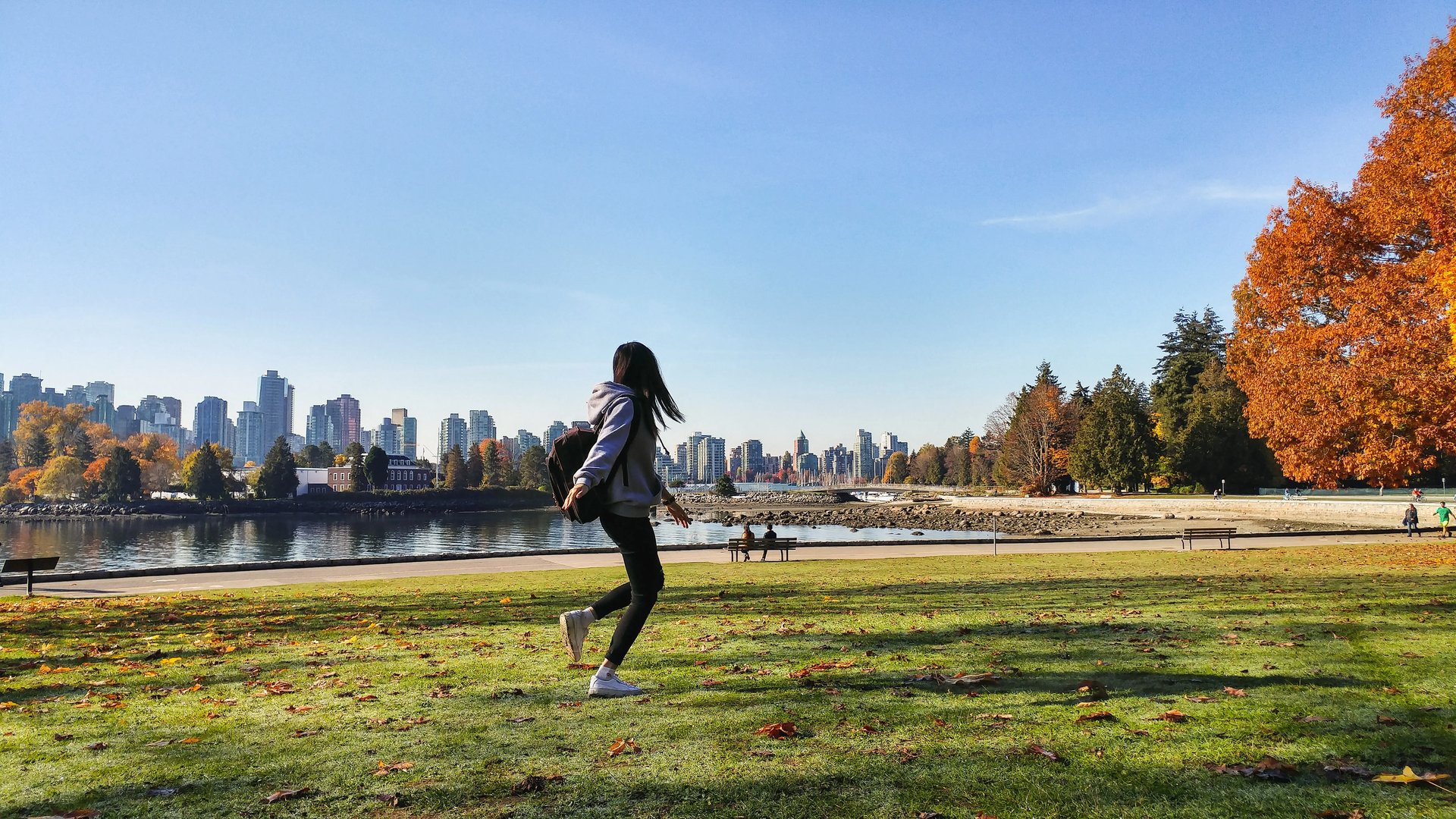 Eine Studentin im Park mit Blick auf die Skyline von Vancouver, umgeben von grünen Wiesen und herbstlichen Bäumen.