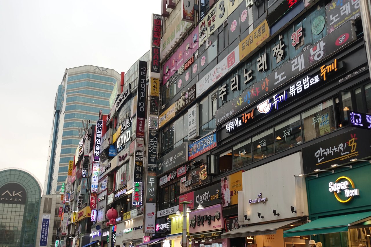 Belebte Einkaufsstraße in Südkorea mit zahlreichen Leuchtreklamen und Schildern.