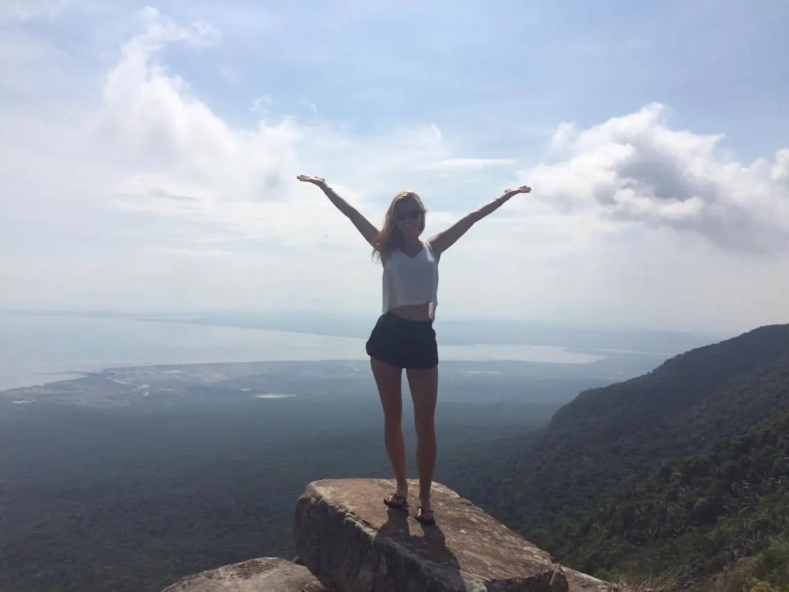 Studentin steht auf einem Felsen und genießt den weiten Ausblick über eine tropische Landschaft in Südostasien.