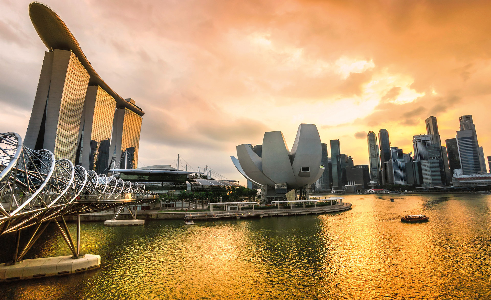 Die Skyline von Singapur bei Sonnenuntergang mit dem berühmten Marina Bay Sands Hotel und der Helix Bridge im Vordergrund. 