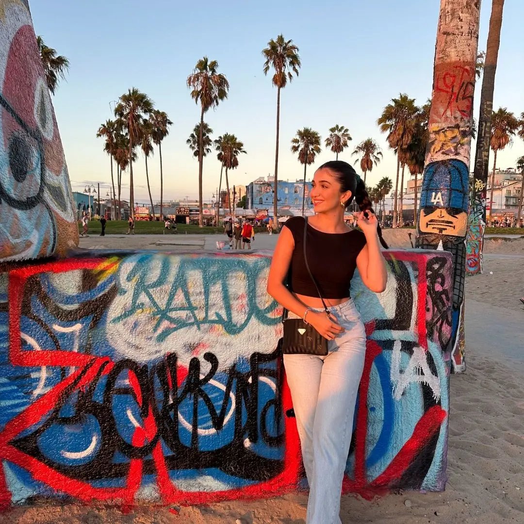 IEC Alumna Suzi lehnt an einer Graffiti-Wand am Strand mit Palmen im Hintergrund. 