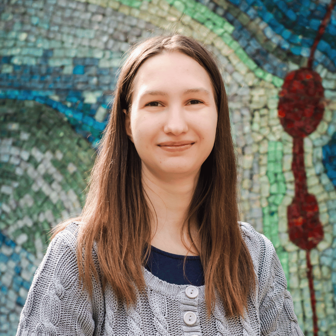 Maria Zasadzki vom IEC Online Team lächelt vor einer bunten Mosaikwand.