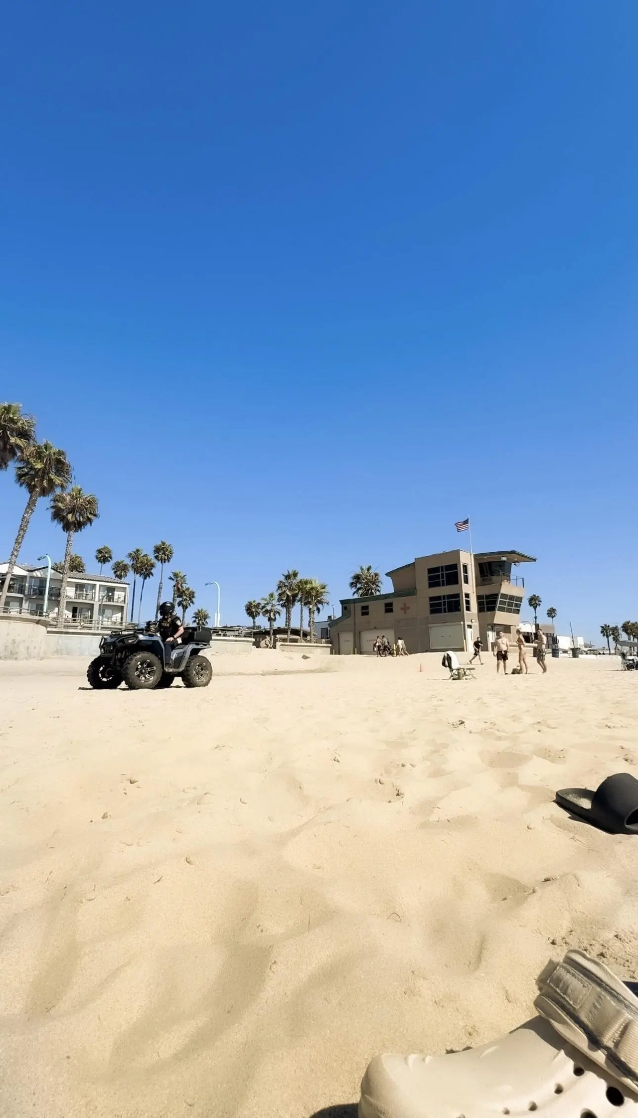 Weißer Sandstrand in Kalifornien mit Palmen, einem Rettungsturm und einem Quadfahrer.