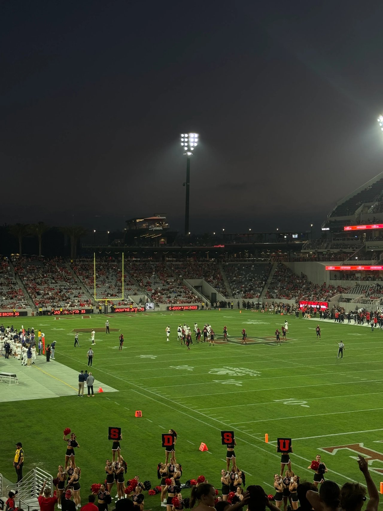 Footballspiel in einem großen Stadion mit Flutlicht, Zuschauern und Cheerleadern.