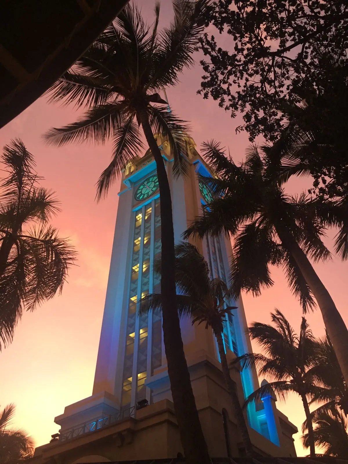 Aloha Tower in Honolulu bei pinkem Sonnenuntergang, umgeben von Palmen.
