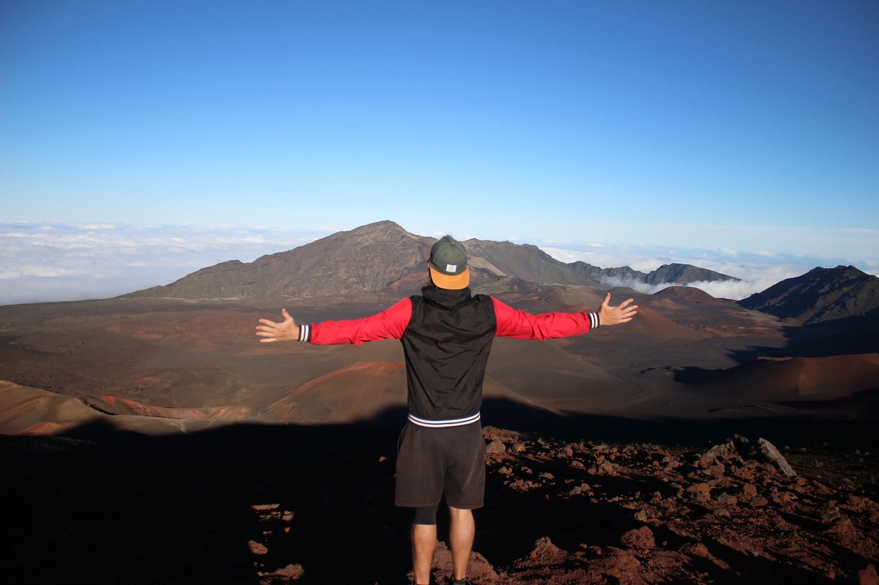 Student mit ausgebreiteten Armen steht auf einem Berg mit Blick auf vulkanische Landschaft Redhill Crater und Wolken.