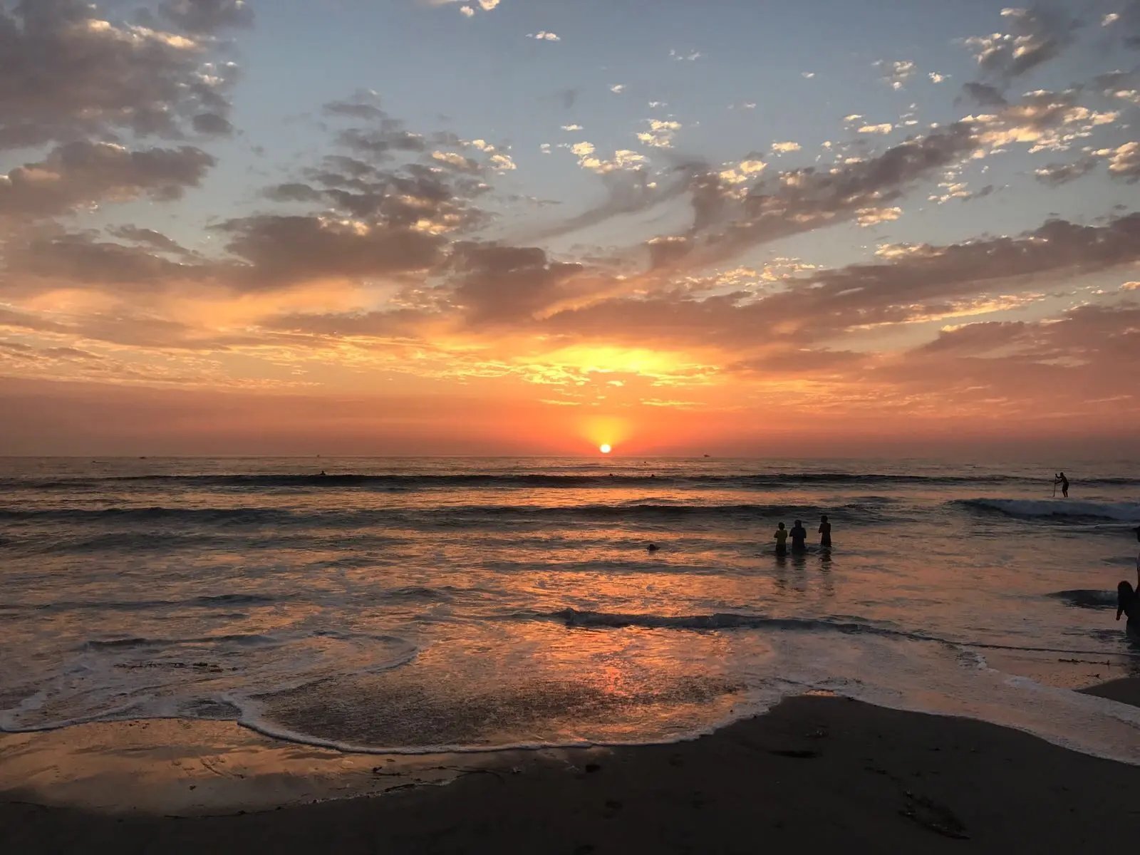 Bild eines farbenfrohen Sonnenuntergangs über dem Meer mit Silhouetten im Wasser.