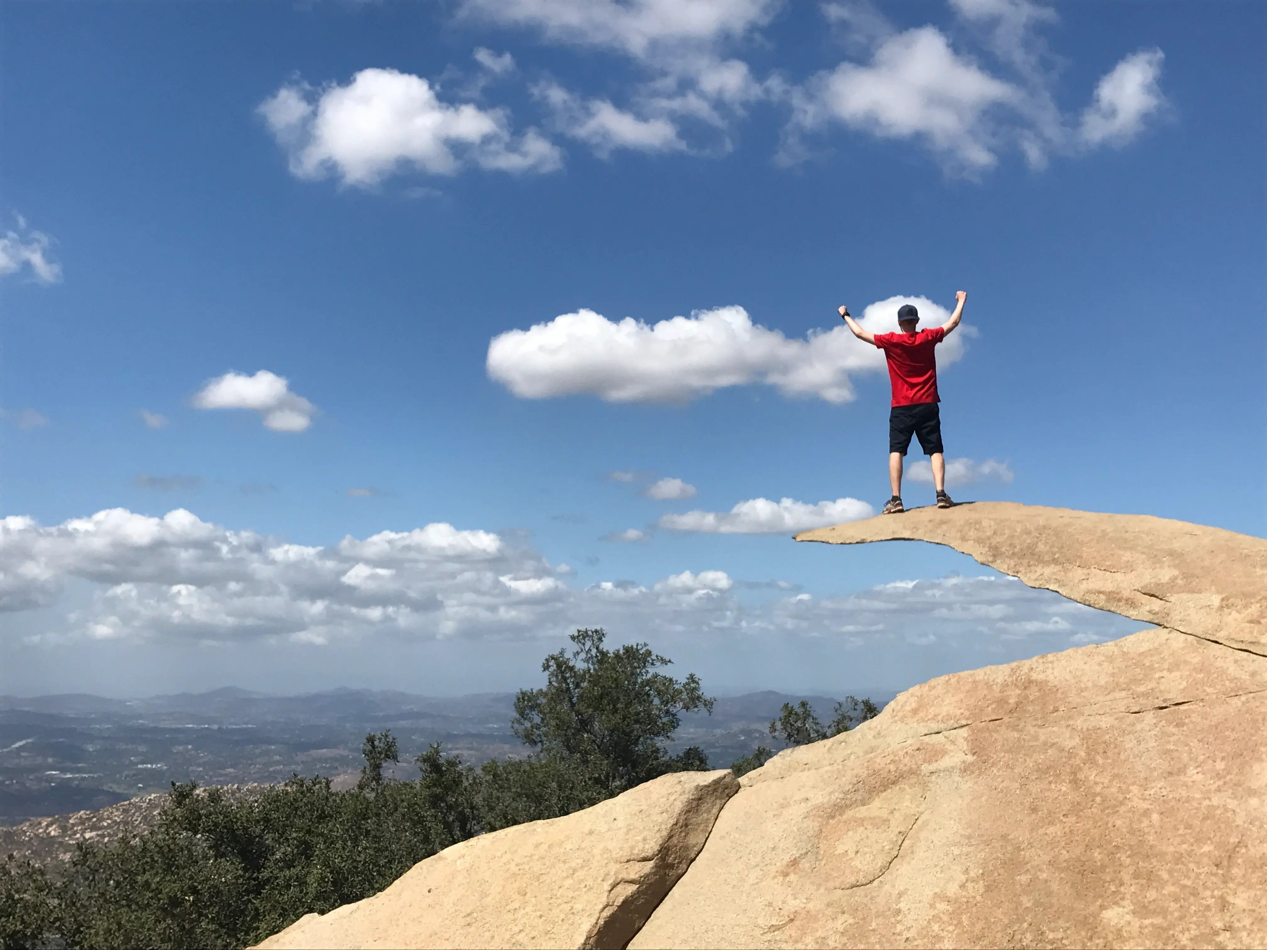 Bild eines Studenten der San Diego State University, der triumphierend auf einem Felsvorsprung mit Blick auf die Berge steht.