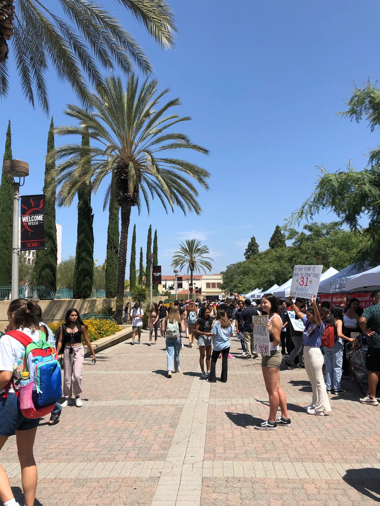 Studenten auf dem belebten Campus der San Diego State University während einer Veranstaltung unter Palmen.