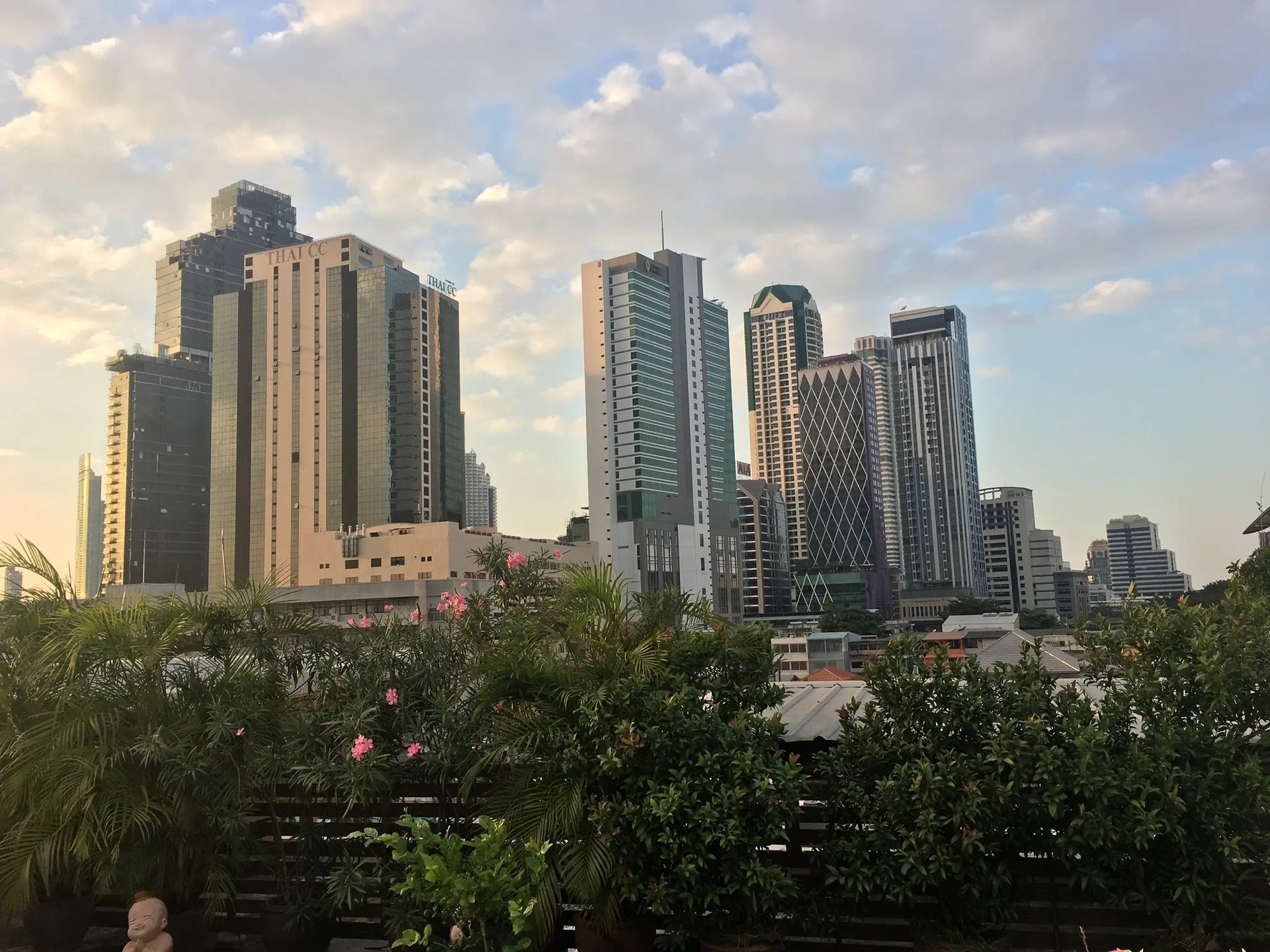 Skyline von Bangkok aufgenommen von einer grünen Dachterrasse mit Blumen.